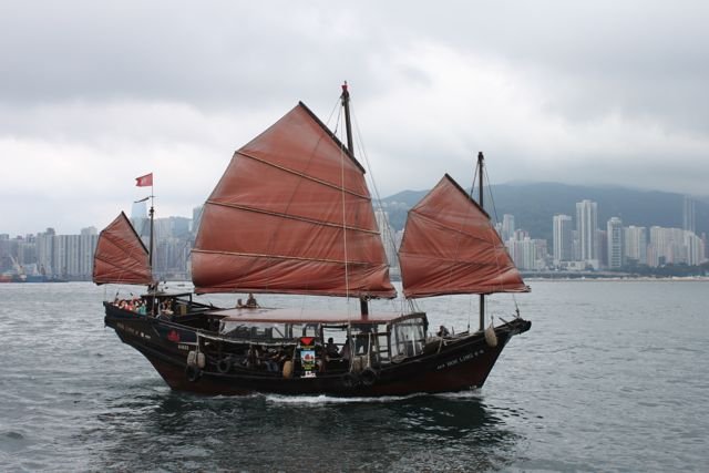 A red-sailed junk crossing Victoria Harbour, with Hong Kong Island beyond
