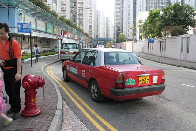 Red Hong Kong taxi on a street with residential towers behind