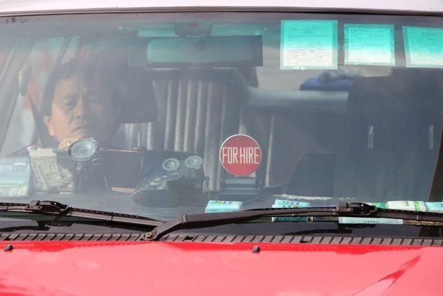 Hong Kong red taxi driver seen through the windscreen with a For Hire sign
