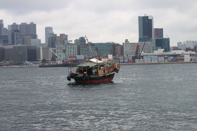 Fishing boat in the harbour with container port and Kowloon skyline behind