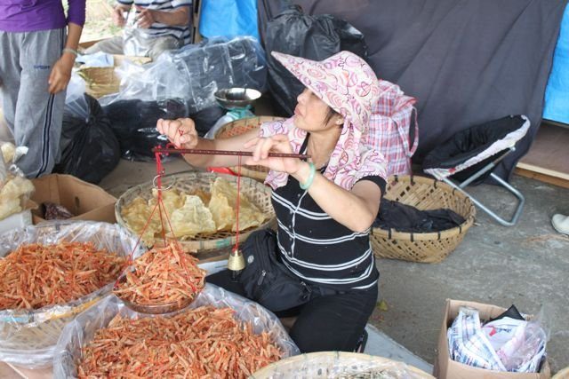 Market vendor weighing dried seafood on a traditional hand scale
