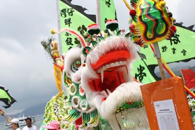 Lion dance head with green flags at a waterfront festival