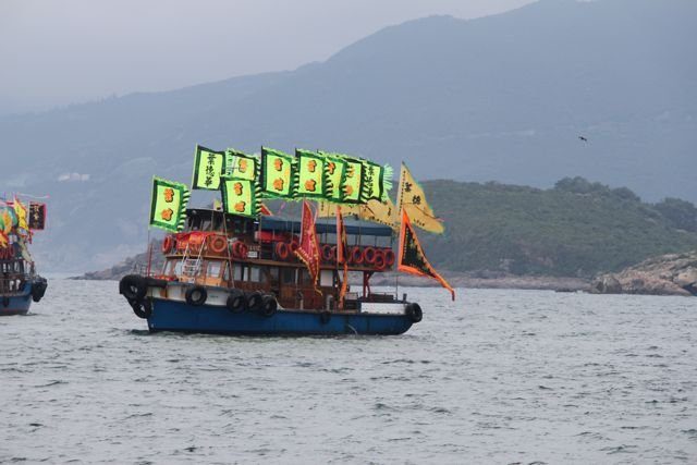 Festival boat covered in flags moored off a hilly island coastline