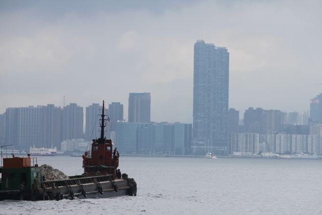Tugboat with a gravel barge in the harbour with Kowloon skyline behind