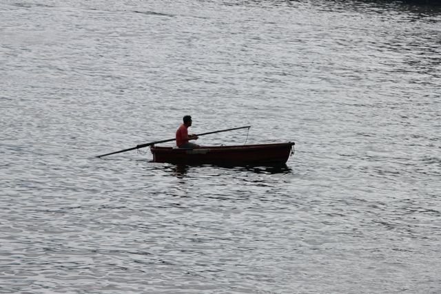 Man rowing a small wooden boat alone in the harbour