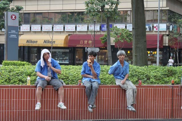 Three workers taking a lunch break on a wall near an MTR station