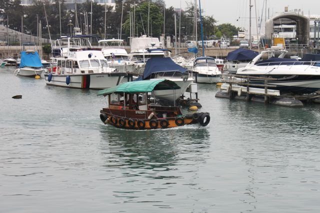 Small sampan boat in a marina surrounded by yachts