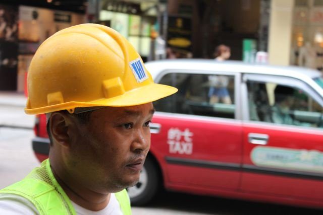 Construction worker in a yellow hard hat with a red taxi passing behind