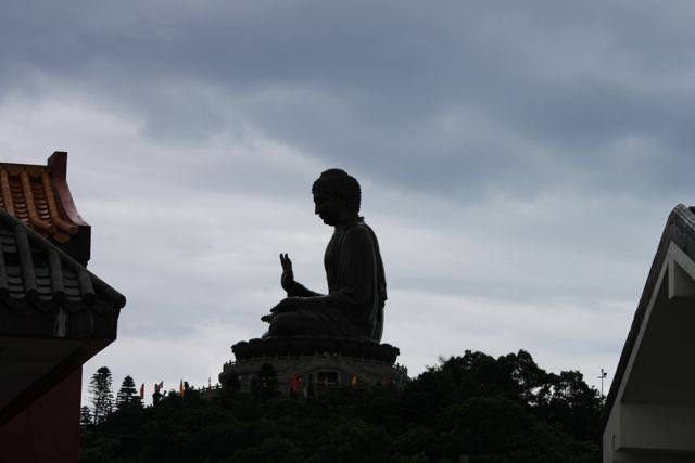 Big Buddha silhouette rising above Po Lin Monastery rooftops