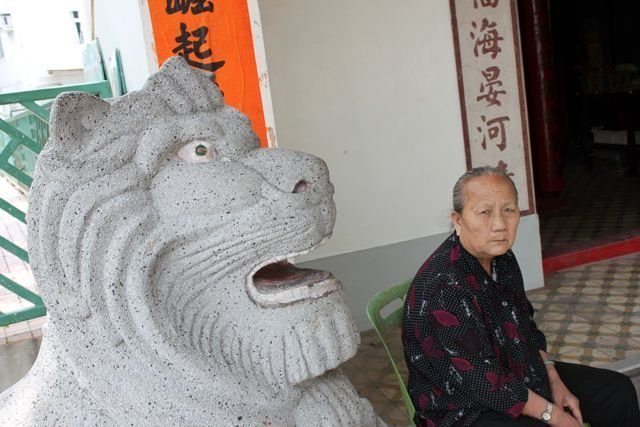 Stone lion statue at a temple entrance with an elderly woman seated nearby