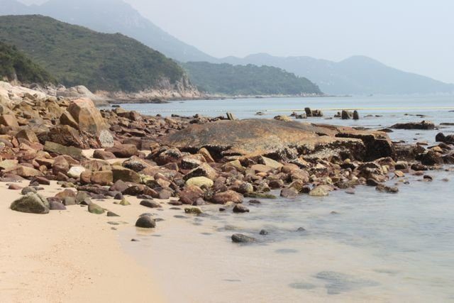Rocky shoreline and sand at low tide with hilly coastline beyond