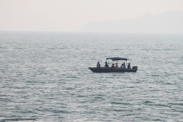 Small boat with passengers on hazy open water with mountains in the distance