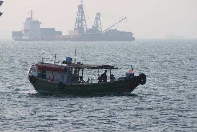 Green fishing boat with industrial cargo ship in the hazy background