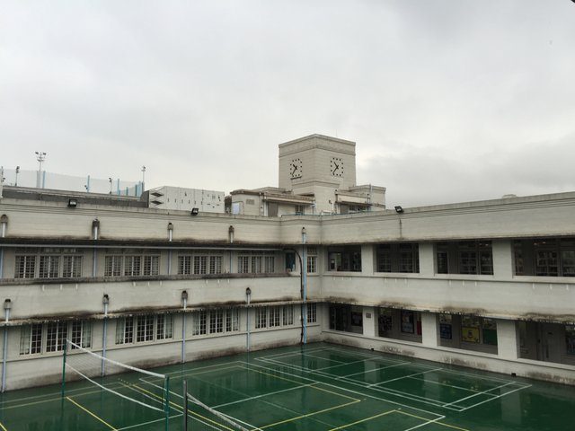 Colonial-era white building with clock tower and rooftop badminton courts, overcast sky