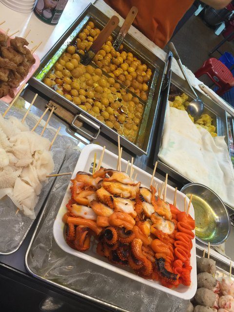 Street food stall with squid skewers and fish balls in sauce trays