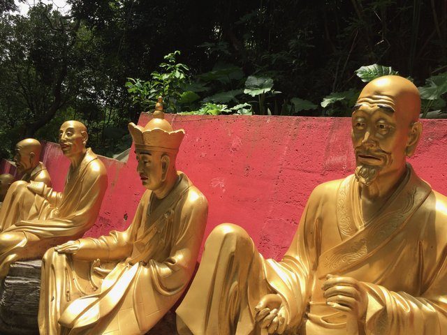 Gold-painted Luohan statues seated against a vivid pink wall at Ten Thousand Buddhas Monastery