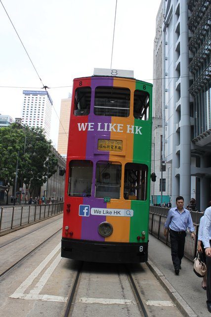Rainbow-wrapped double-decker tram reading We Like HK on a city street