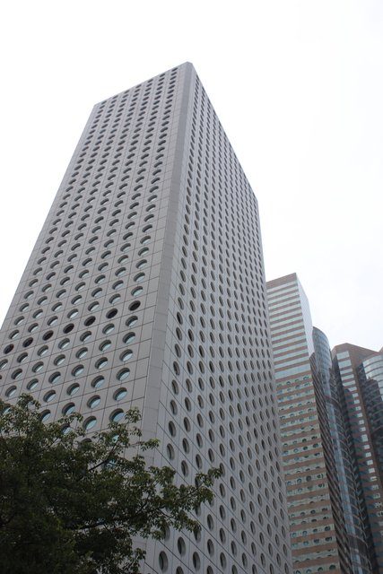 Unusual circular-windowed skyscraper facade seen from street level, overcast sky