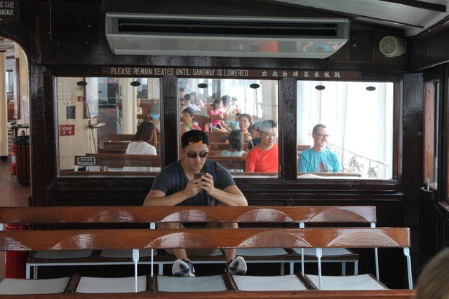 Passengers on the Star Ferry's wooden benches, bilingual notice on the partition