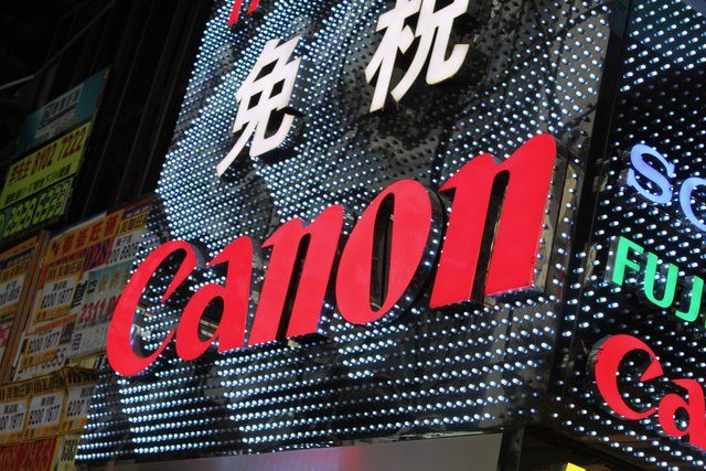 Illuminated Canon sign blazing red against a glittering LED billboard at night