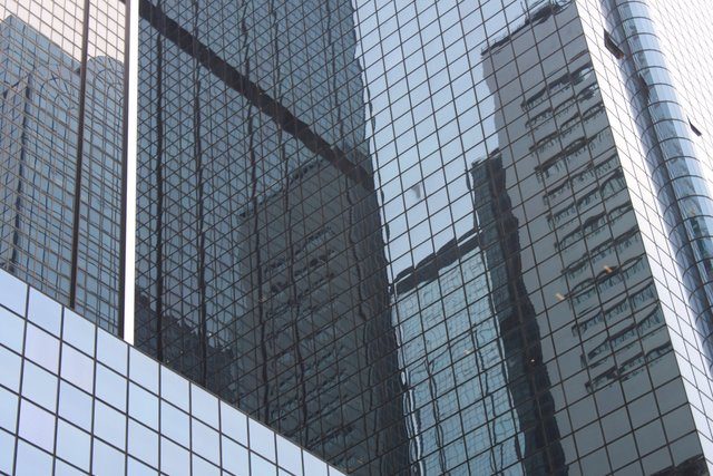 Adjacent glass towers reflecting each other's facades in distorted blue panels