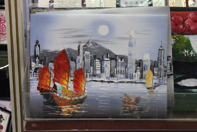 Painted souvenir canvas showing red-sailed junks against a grey harbour skyline