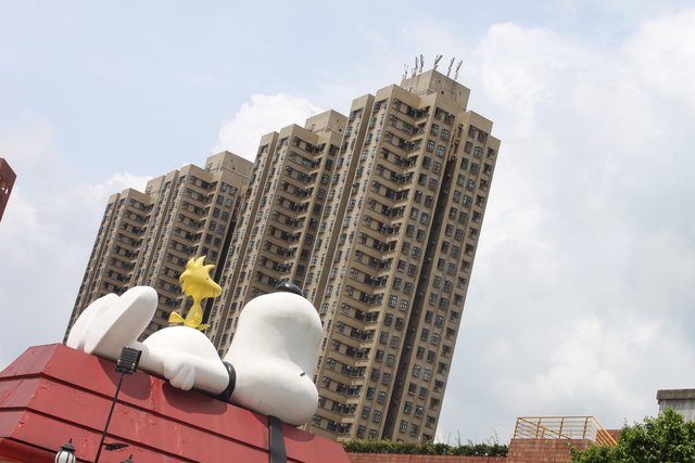 Snoopy and Woodstock figures atop a kennel with residential towers behind