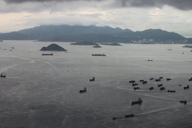 Cargo ships scattered across a wide grey bay, islands and mountains beyond