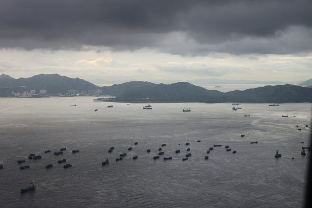 Dozens of vessels at anchor in a storm-lit strait, dark clouds over the hills