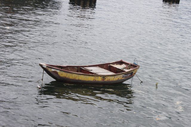 Battered yellow and red wooden rowing boat moored on calm grey water