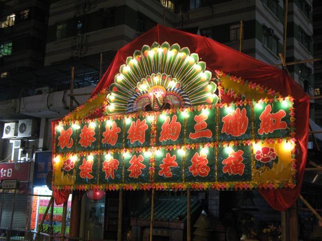 Illuminated festival shrine with Chinese characters and peacock decoration at night
